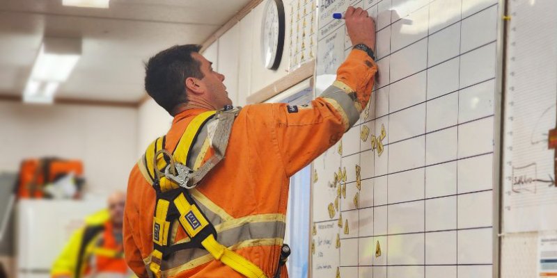 Man wearing safety equipment writing on Critical Risk Management whiteboard