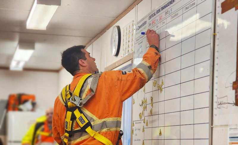 Man wearing safety equipment writing on Critical Risk Management whiteboard